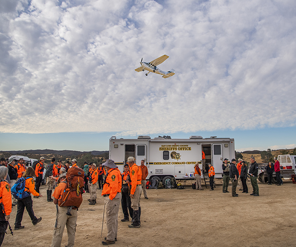 Search and Rescue volunteers with Search and Rescue trailer and Aero plane flying overhead.