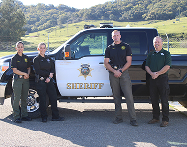 Four Behavioral Health Community Action Team members standing with a Sheriff's Office truck smiling forward.