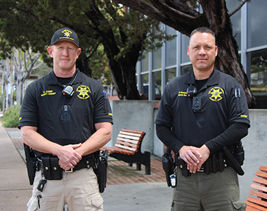 Two Civil Deputies standing in front of the County Courthouse looking at the camera.