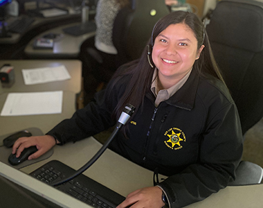 Dispatcher sitting at a work station with a microphone and keyboard and looking straight forward smiling.