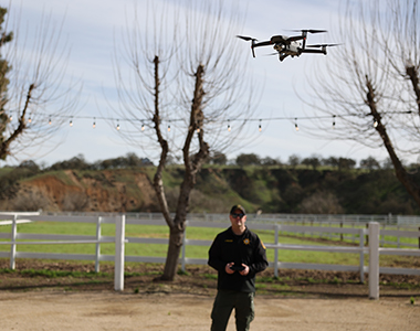 Drone flying with Drone Team member standing in the background with a controller.