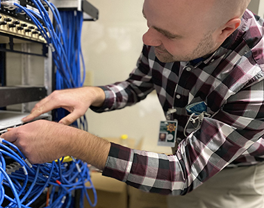 Sheriff's Office Systems Administrator working with blue cords.