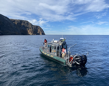 Sheriff's Office boat in the ocean with a large rock in the background and team members seen on the boat working.