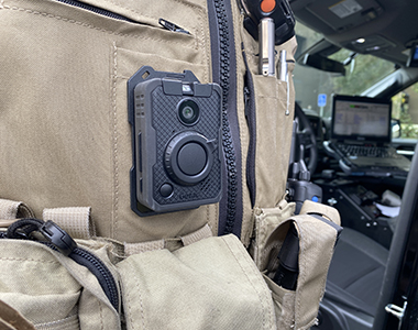 Body-Worn Camera on a deputy close up with interior of a patrol vehicle in the background.