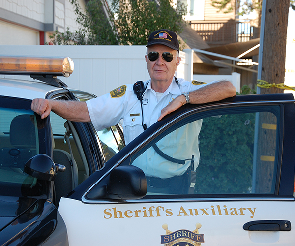 Sheriff's Auxiliary Volunteer Patrol member leaning on the door of a volunteer patrol vehicle.