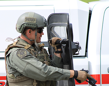 SED member holding a shield and gun while looking through the shield.
