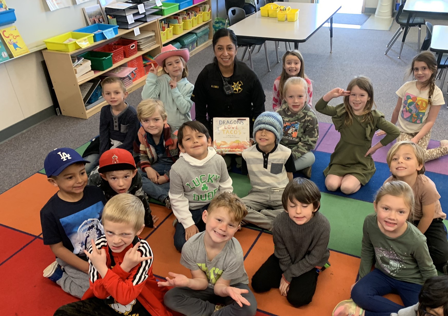 School Resource Deputy sitting holding a book surrounded by students in a classroom.