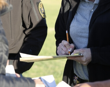 Clipboard held with someone writing with a pencil.